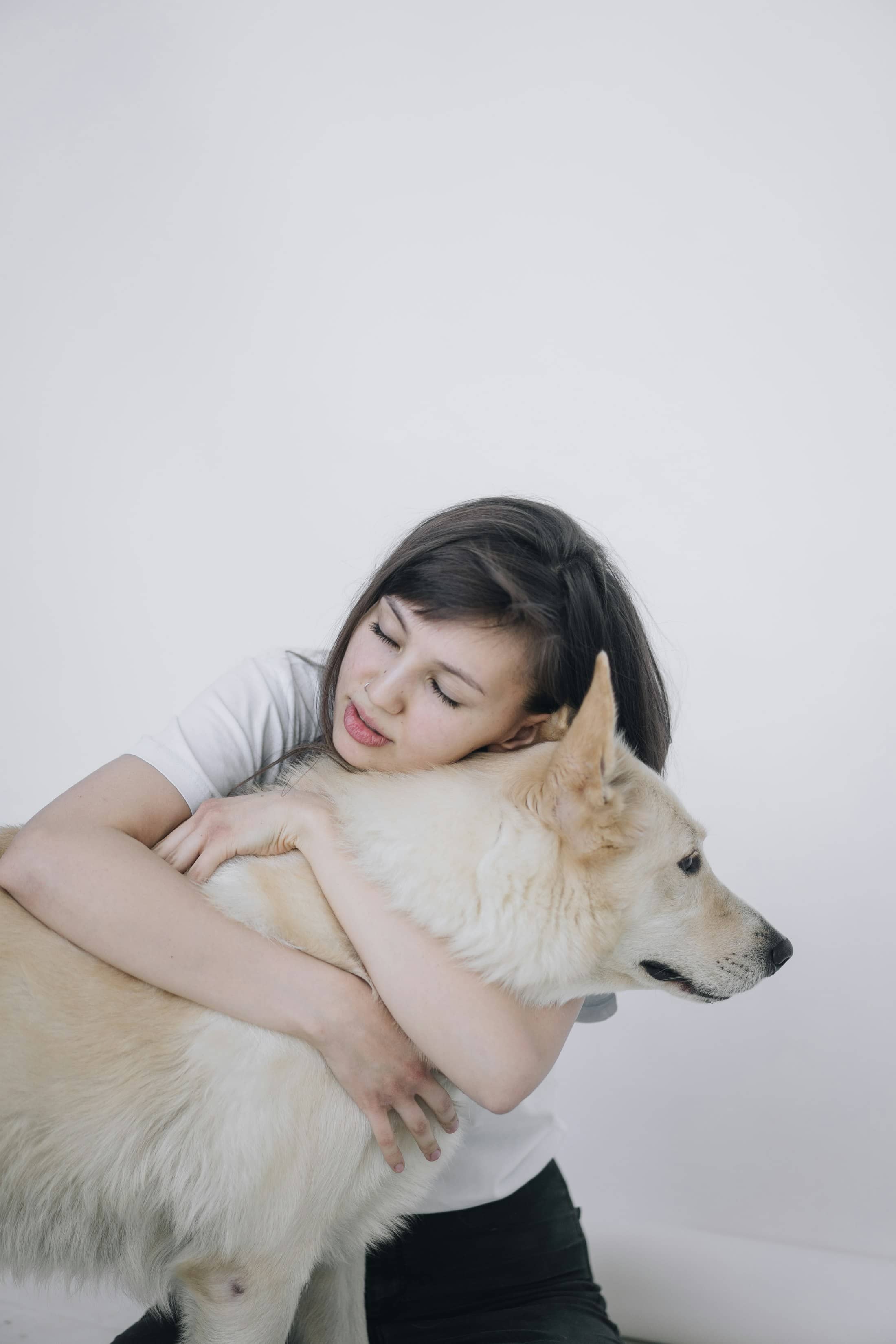 Mulher de olhos fechados abraçando um cachorro de pelo claro